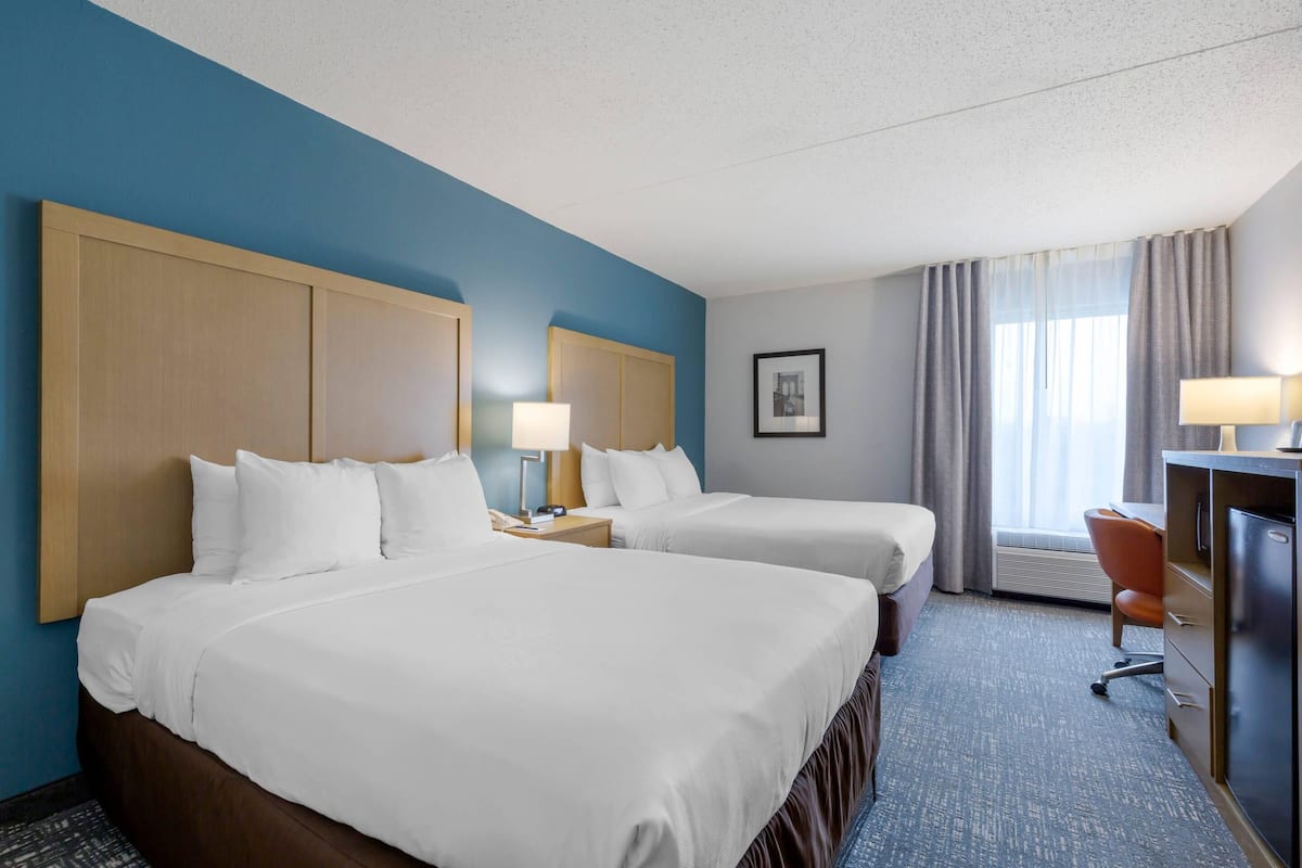 A hotel room with two beds, a desk, a chair, and a window with curtains.