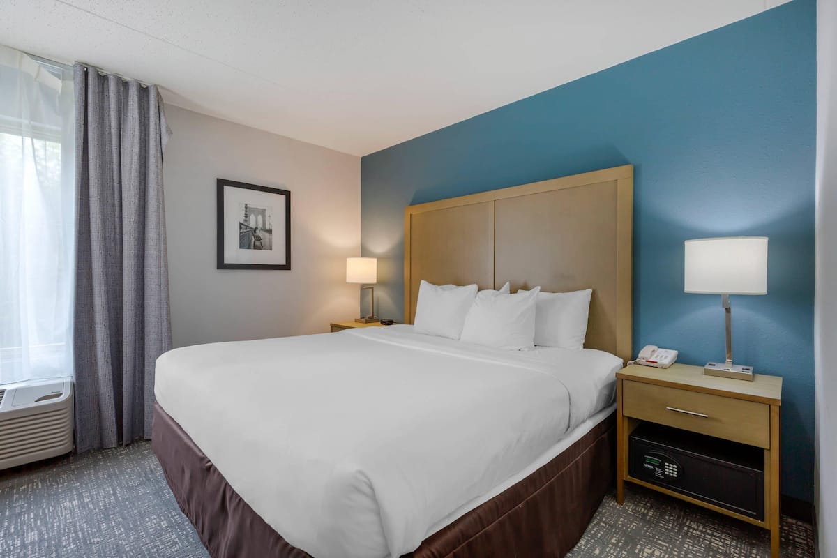 A hotel room with a large bed, bedside tables with lamps, a framed picture on the wall, and a window with curtains.