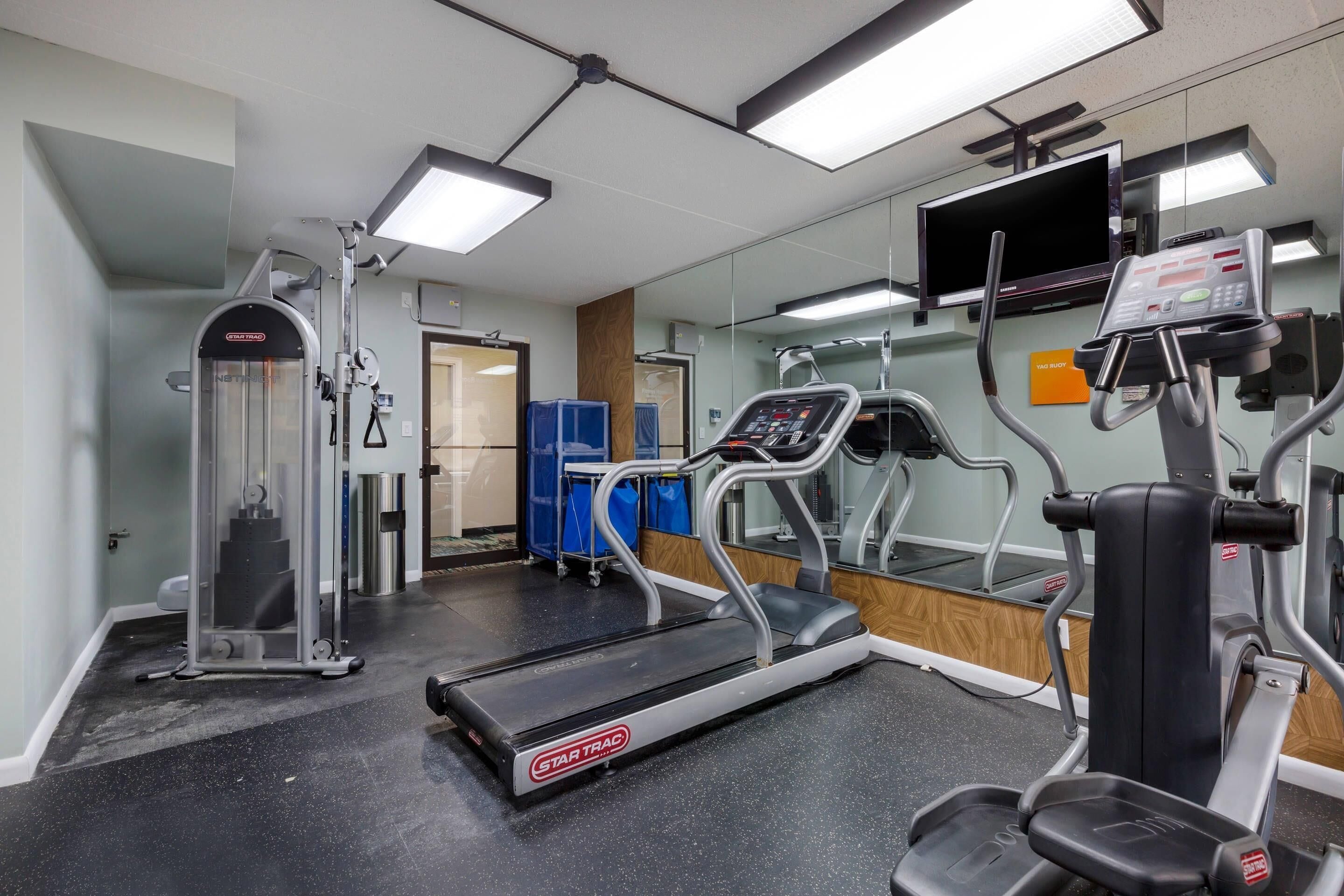 A gym with a treadmill, elliptical, and weight machine.