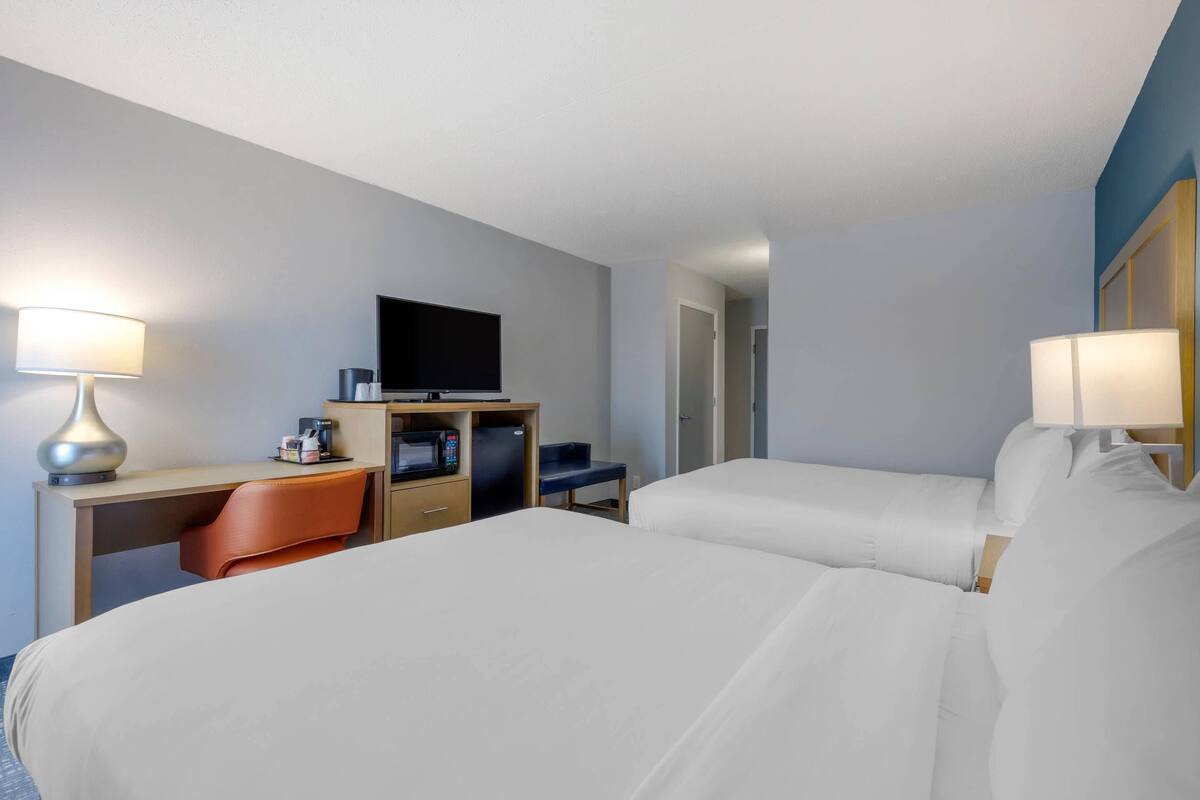 A hotel room with two beds, a desk with a chair, a television, and a minibar.
