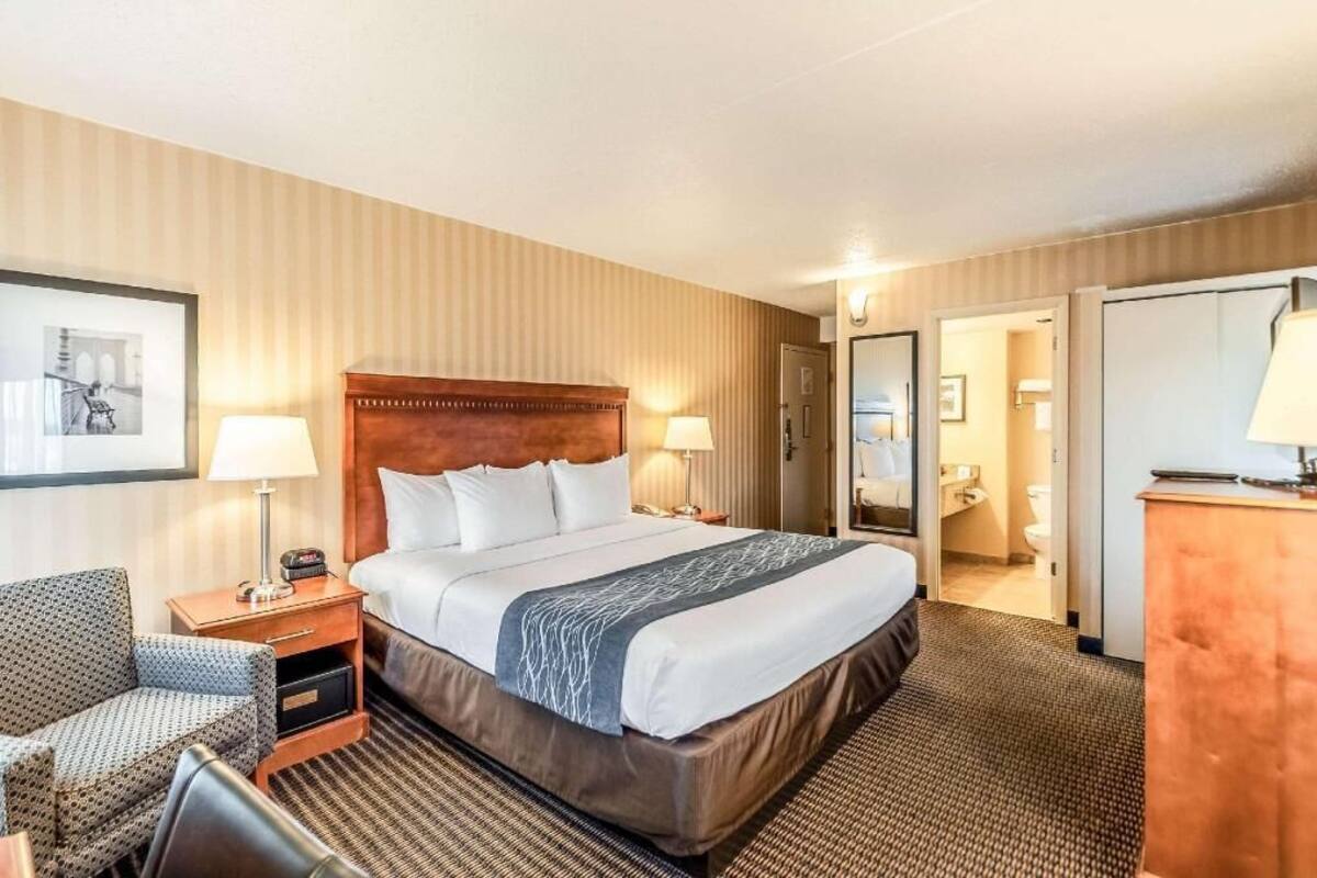 A hotel room with a large bed, bedside tables, a chair, a desk, and a mirror.