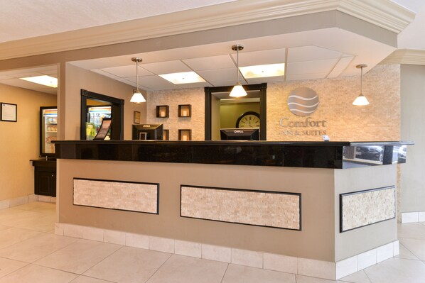 A hotel reception desk with a clock, framed pictures, and a sign for 'Comfort Inn & Suites'. - Comfort Inn & Suites Alexandria West (Alexandria)