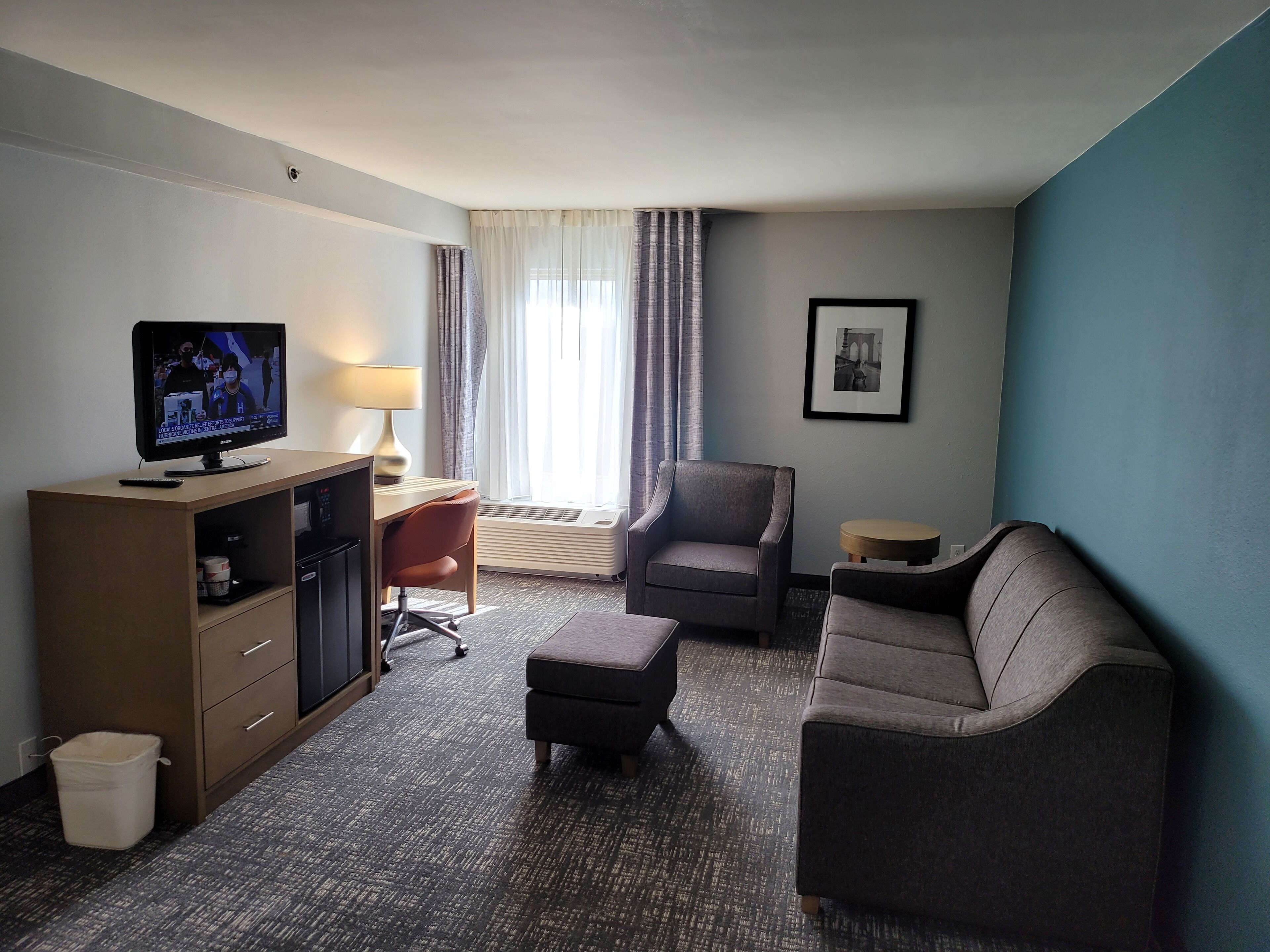 Una habitación de hotel con televisión, escritorio, silla, sofá y aire acondicionado.