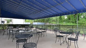 An outdoor patio area with metal tables and chairs, covered by a blue canopy.