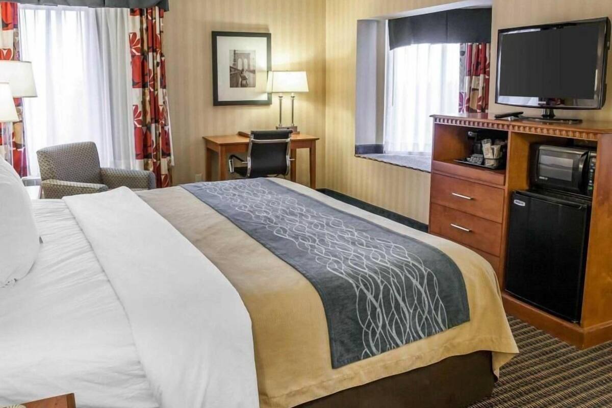 A hotel room with a bed, desk, chair, television, and a small refrigerator.