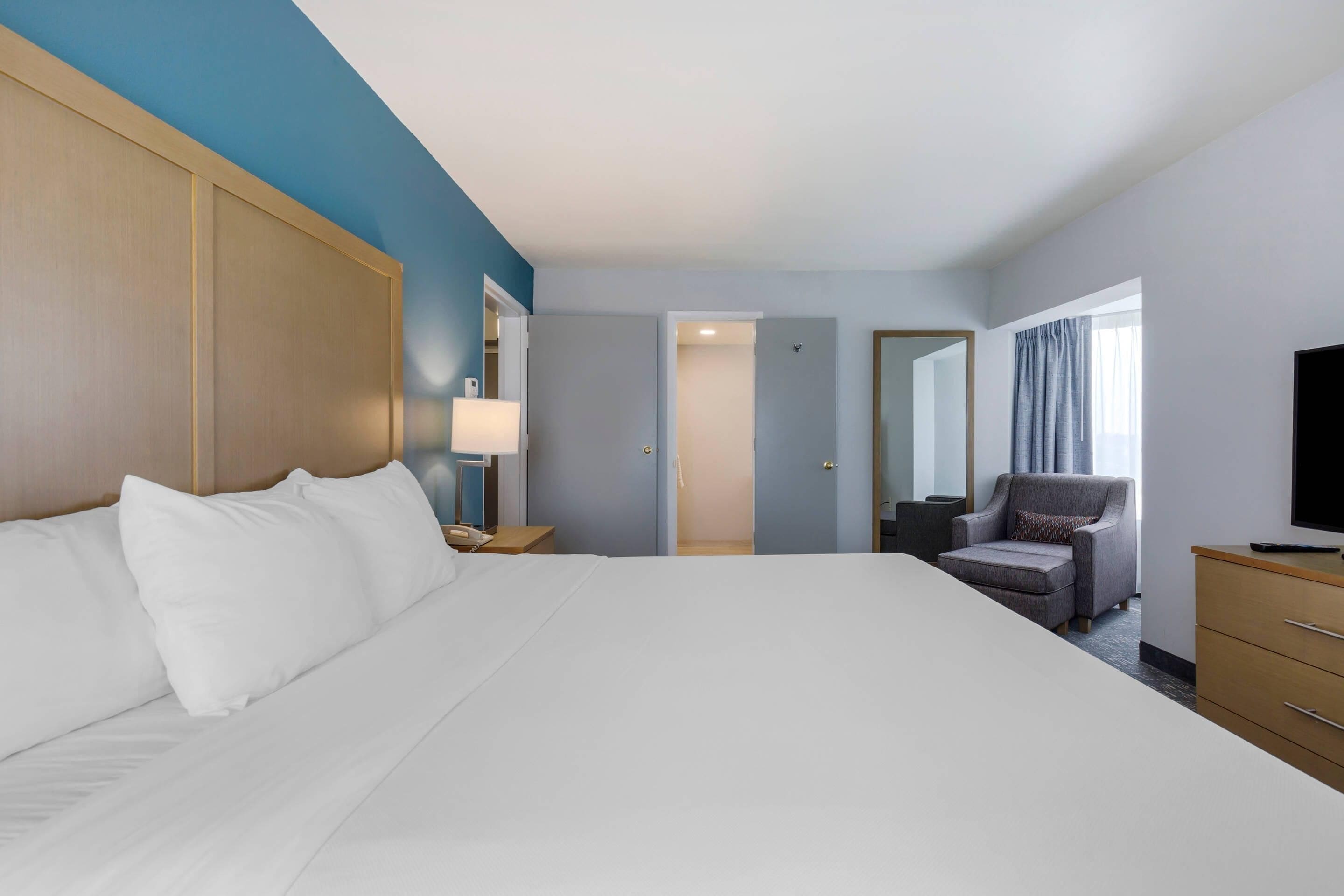 A hotel room with a large bed, a desk with a lamp, a chair, a TV, and a wardrobe.