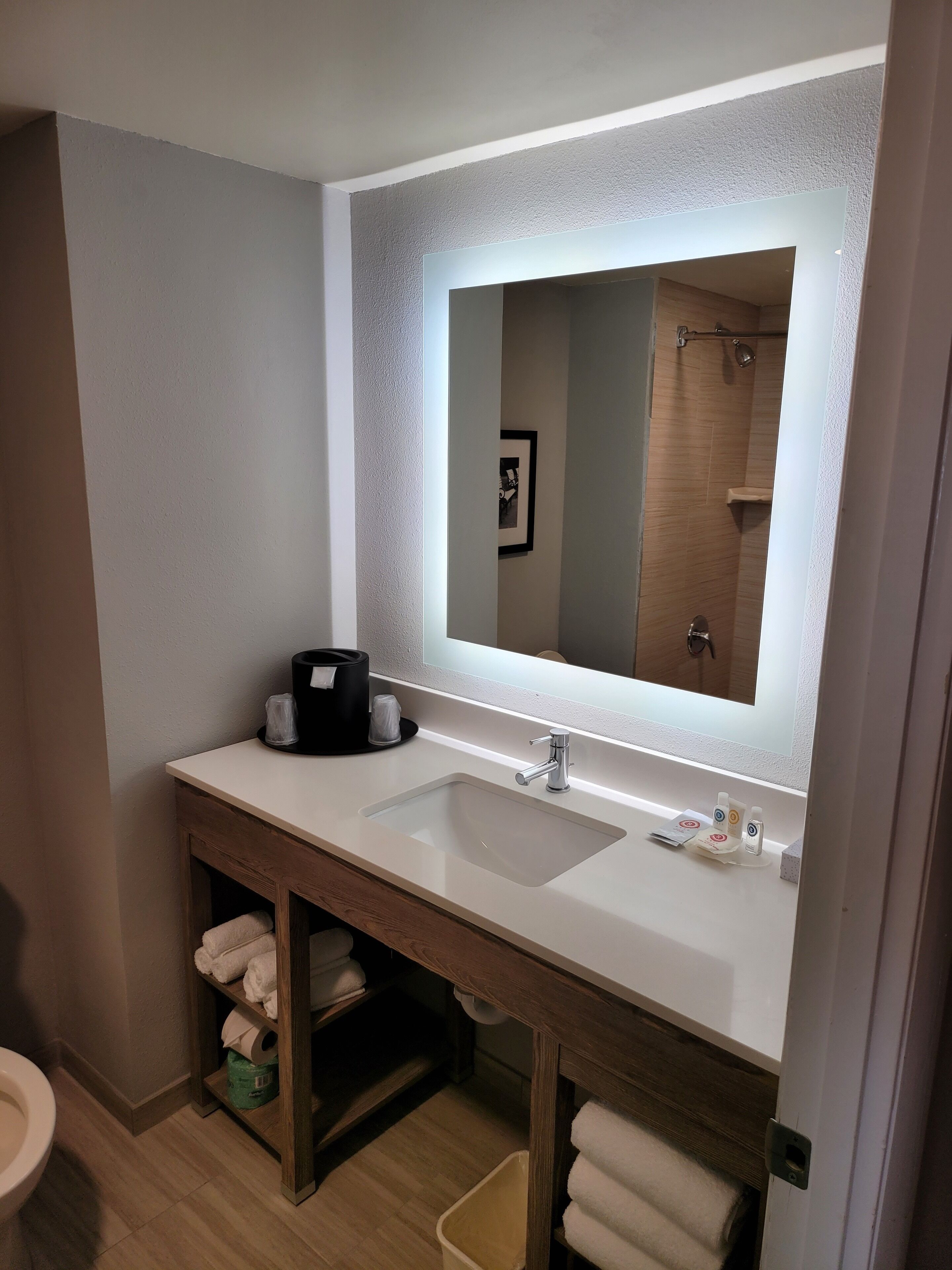 Ein modernes Badezimmer mit einem großen Spiegel, zwei Waschbecken, einem Handtuchhalter und einer in der Spiegelung sichtbaren Dusche.
