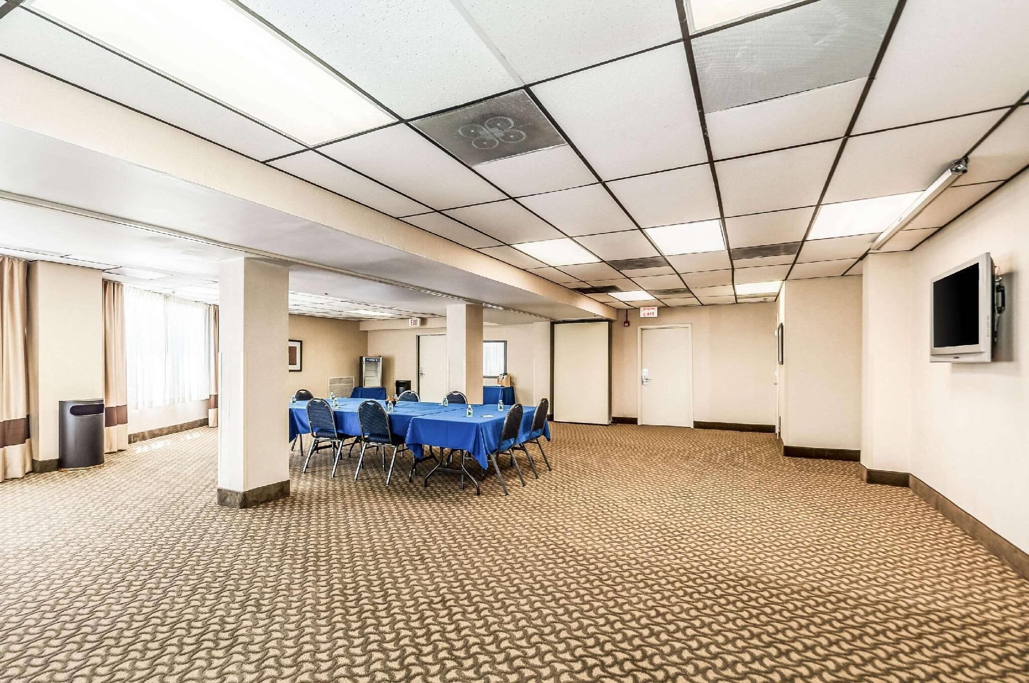 A conference room with a carpeted floor, a long table with chairs, and a flat-screen TV on the wall.