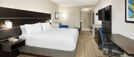 Una habitación de hotel con cama, mesita de noche, lámpara, escritorio, silla y televisor.