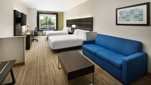 Ein Hotelzimmer mit einem Bett, einem blauen Sofa, einem Schreibtisch mit Computer, einem Fernseher und einem gerahmten Bild an der Wand.