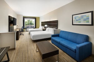 Una habitación de hotel con una cama, un sofá azul, un escritorio con una computadora, un televisor y un cuadro en la pared.