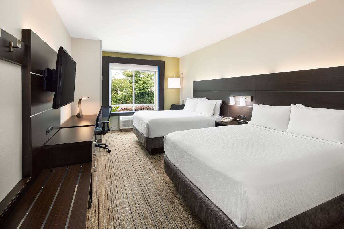 Une chambre d’hôtel avec deux lits, une télévision, un bureau et une fenêtre donnant sur des arbres.