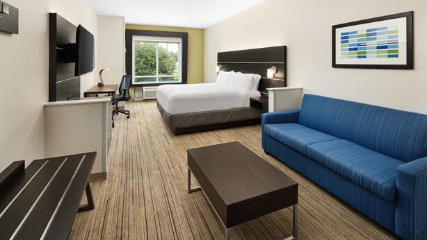 Ein Hotelzimmer mit einem Bett, einem blauen Sofa, einem Schreibtisch mit Stuhl, einem an der Wand montierten Fernseher und einem gerahmten Bild.