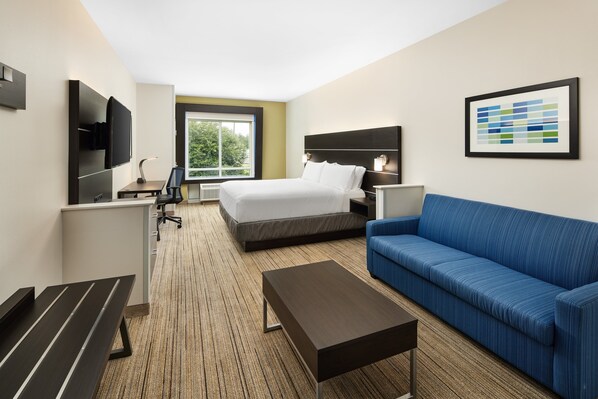 A hotel room with a bed, a blue sofa, a desk with a chair, a TV mounted on the wall, and a framed picture on the wall. - Holiday Inn Express & Suites Valdosta West - Mall Area by IHG (Valdosta)