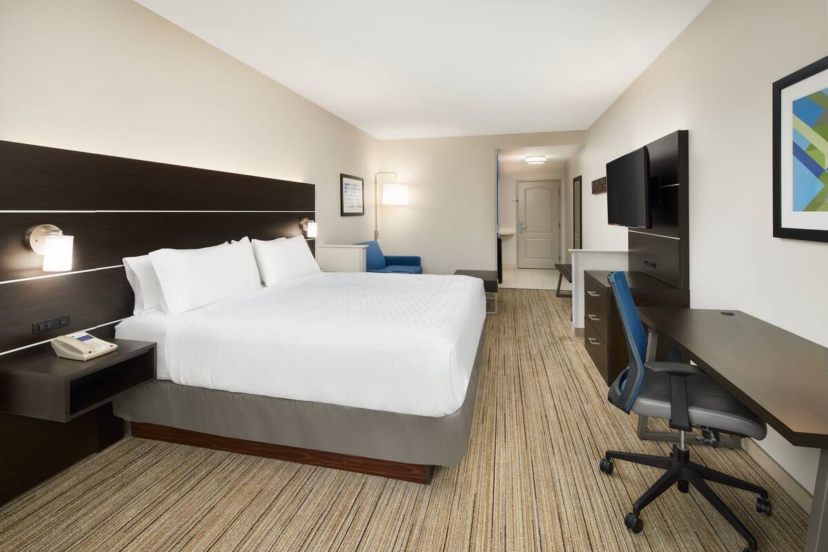 Une chambre d’hôtel avec un grand lit, une table de chevet avec un téléphone, un bureau avec une chaise, un téléviseur à écran plat et un téléviseur fixé au mur.