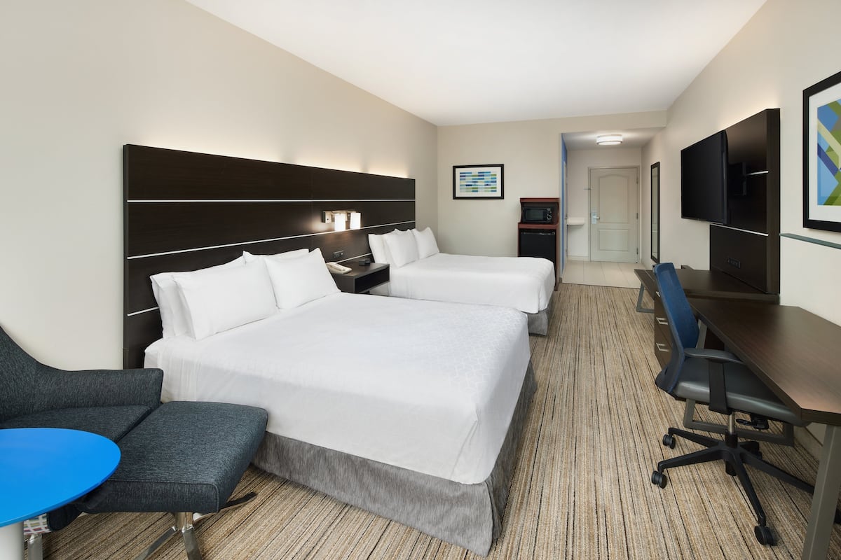 Une chambre d’hôtel avec deux lits, un bureau, une chaise, une télévision et une petite kitchenette.