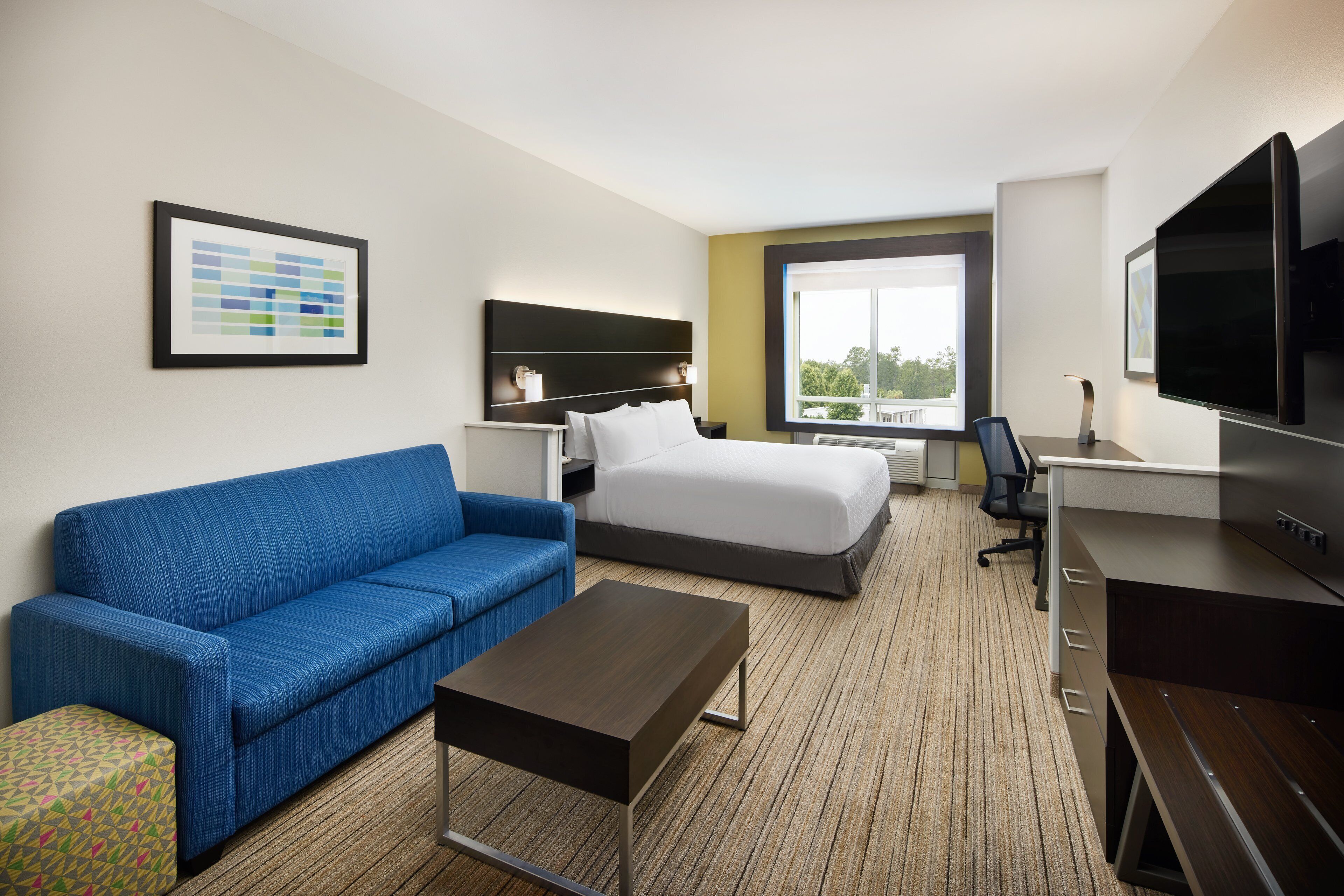 A hotel room with a blue sofa, a bed, a desk, and a TV.