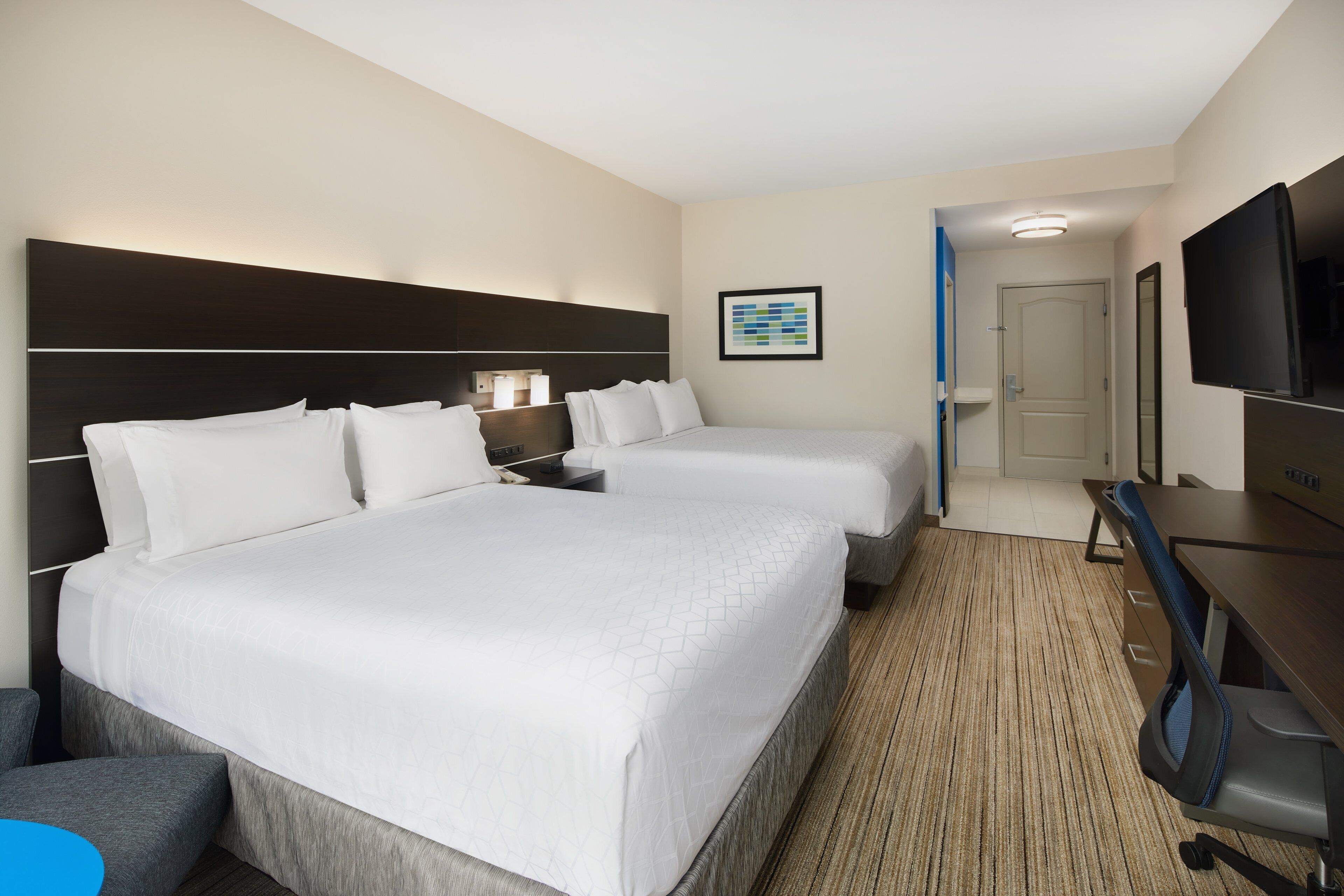 A hotel room with two beds, a desk, a TV, and a bathroom visible through an open door.