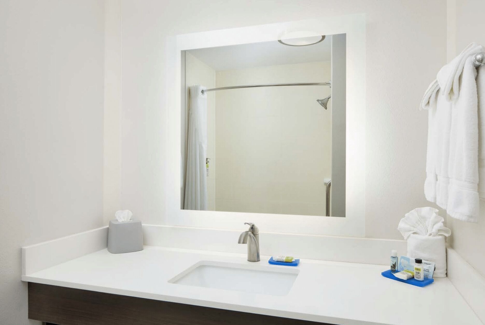 A bathroom with a white sink, a mirror, a towel rack, and toiletries on the counter.