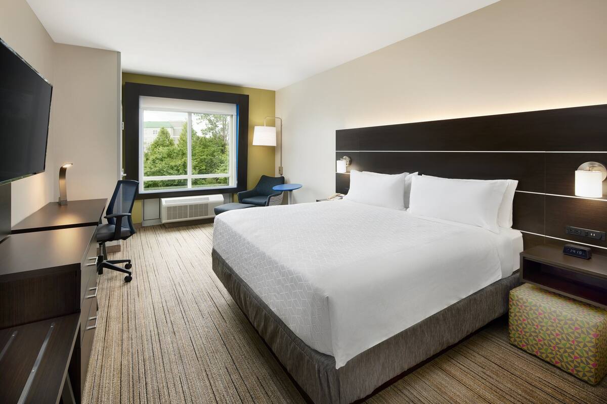 Une chambre d’hôtel avec un grand lit, un bureau, une chaise, une petite table, une télévision et une fenêtre donnant sur des arbres.