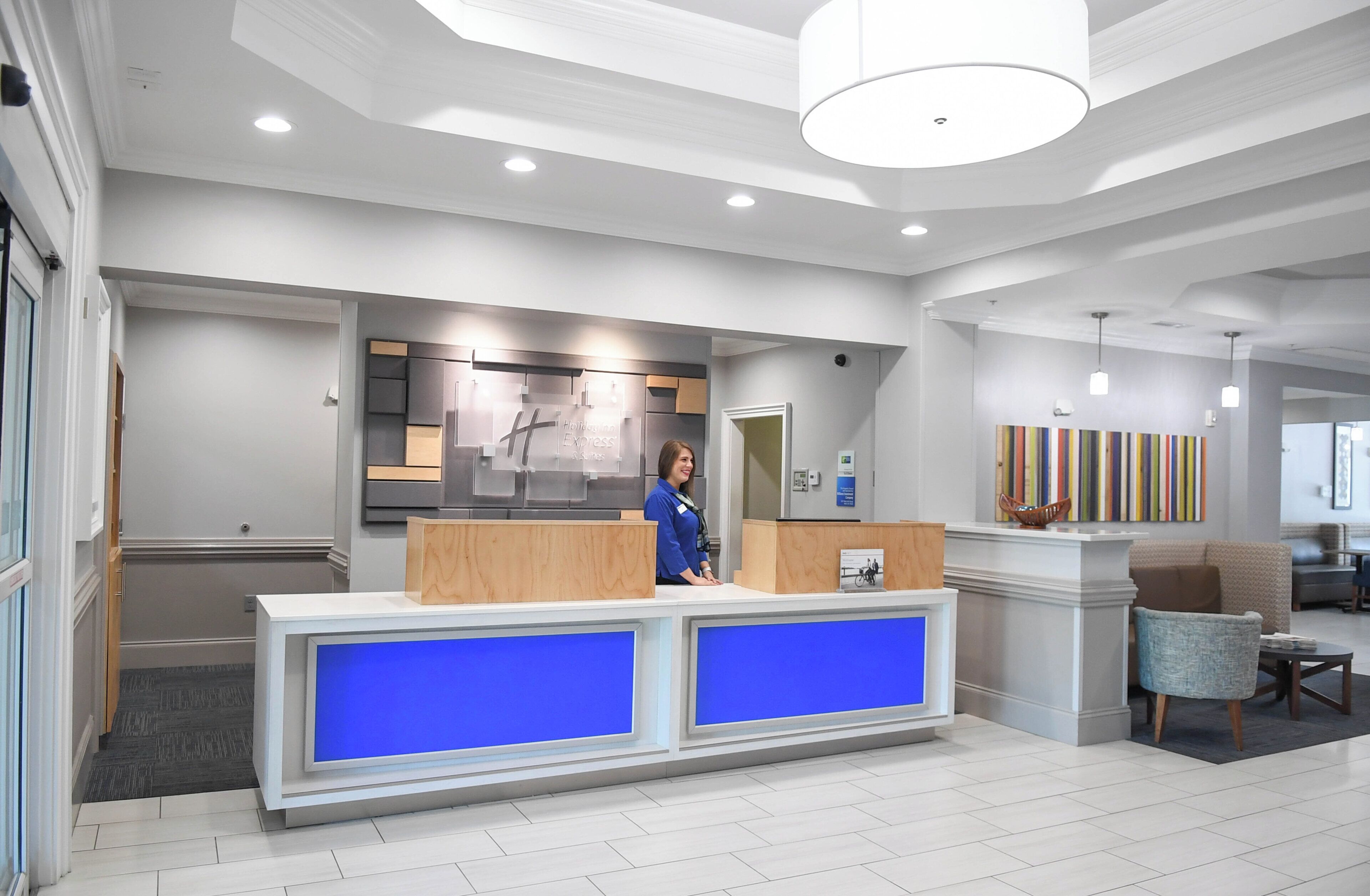 A modern reception desk with a blue accent, a person standing behind it, and a large artwork on the wall.