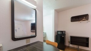 Ein kleiner, moderner Raum mit einem Holztisch, einem Spiegel, einem Fernseher und einer kleinen Küchenzeile.