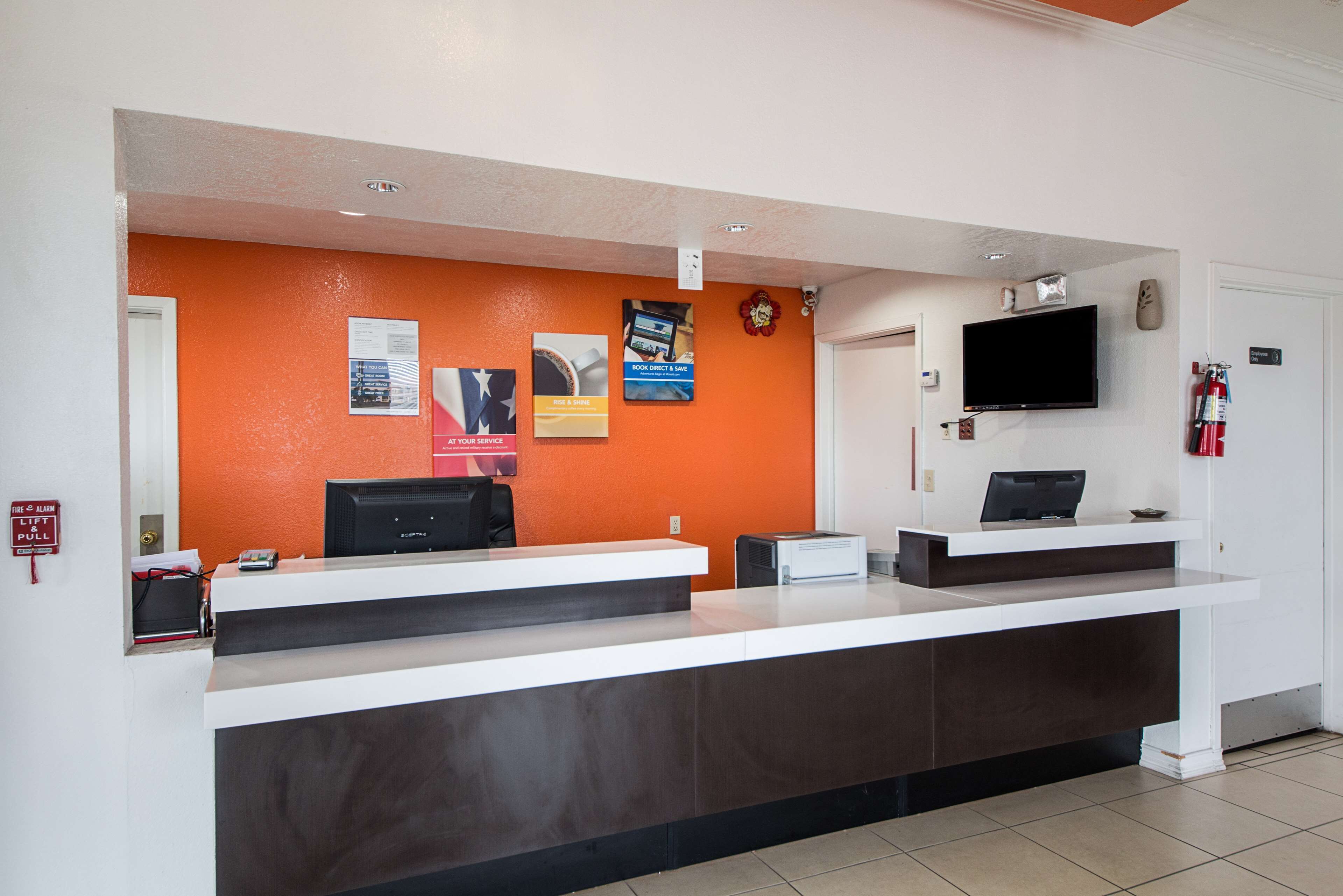 A reception desk with a flat-screen TV, a fire alarm pull station, and a fire extinguisher.