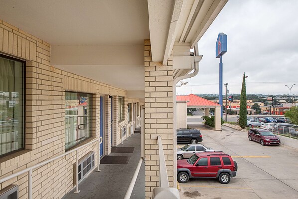 Un motel con fachada de ladrillo, una zona de estacionamiento techada y vistas a la calle con coches aparcados.