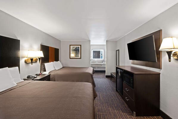 A hotel room with two beds, a TV, a desk with a lamp, a mirror, and a window.