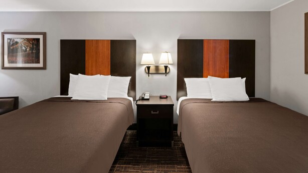 A hotel room with two beds, a nightstand with a lamp, and a framed picture on the wall. - Best Western Executive Inn (Grove City)
