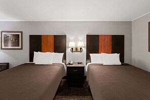 A hotel room with two beds, a nightstand with a lamp, and a framed picture on the wall.