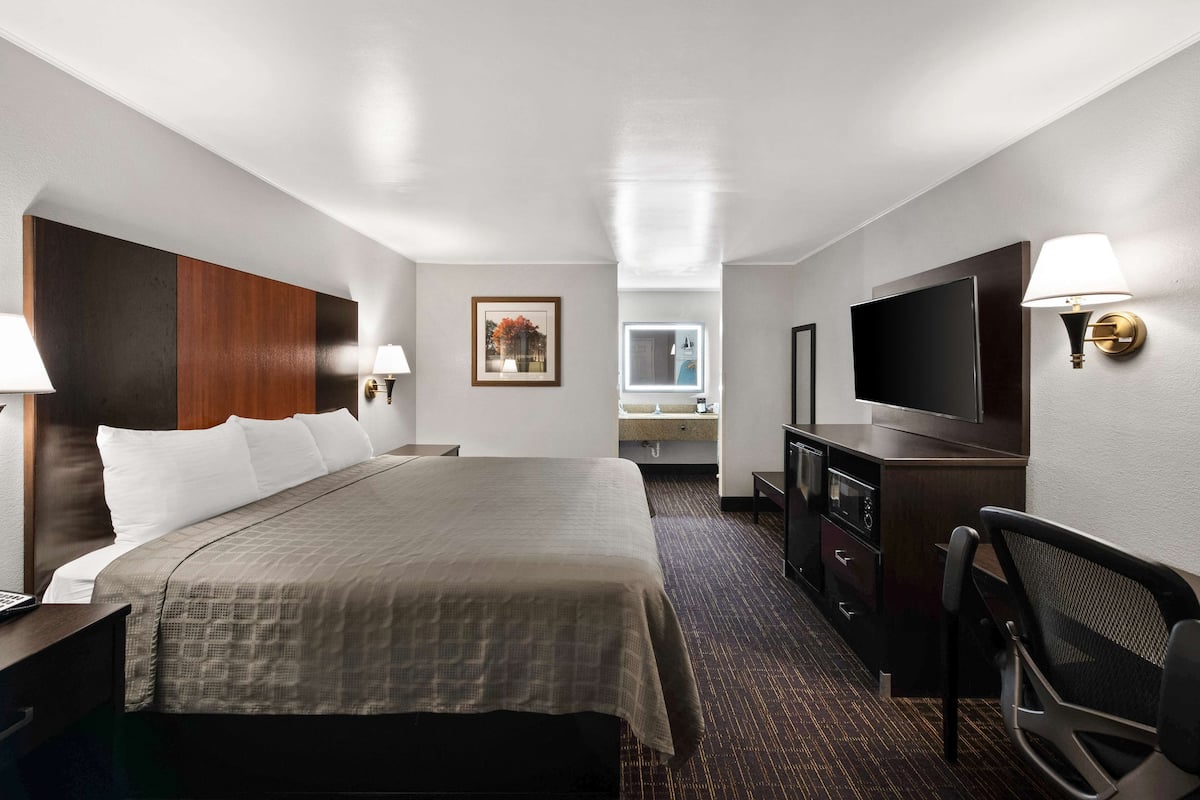 A hotel room with a large bed, a desk, a television, a mirror, and a bathroom visible in the background.