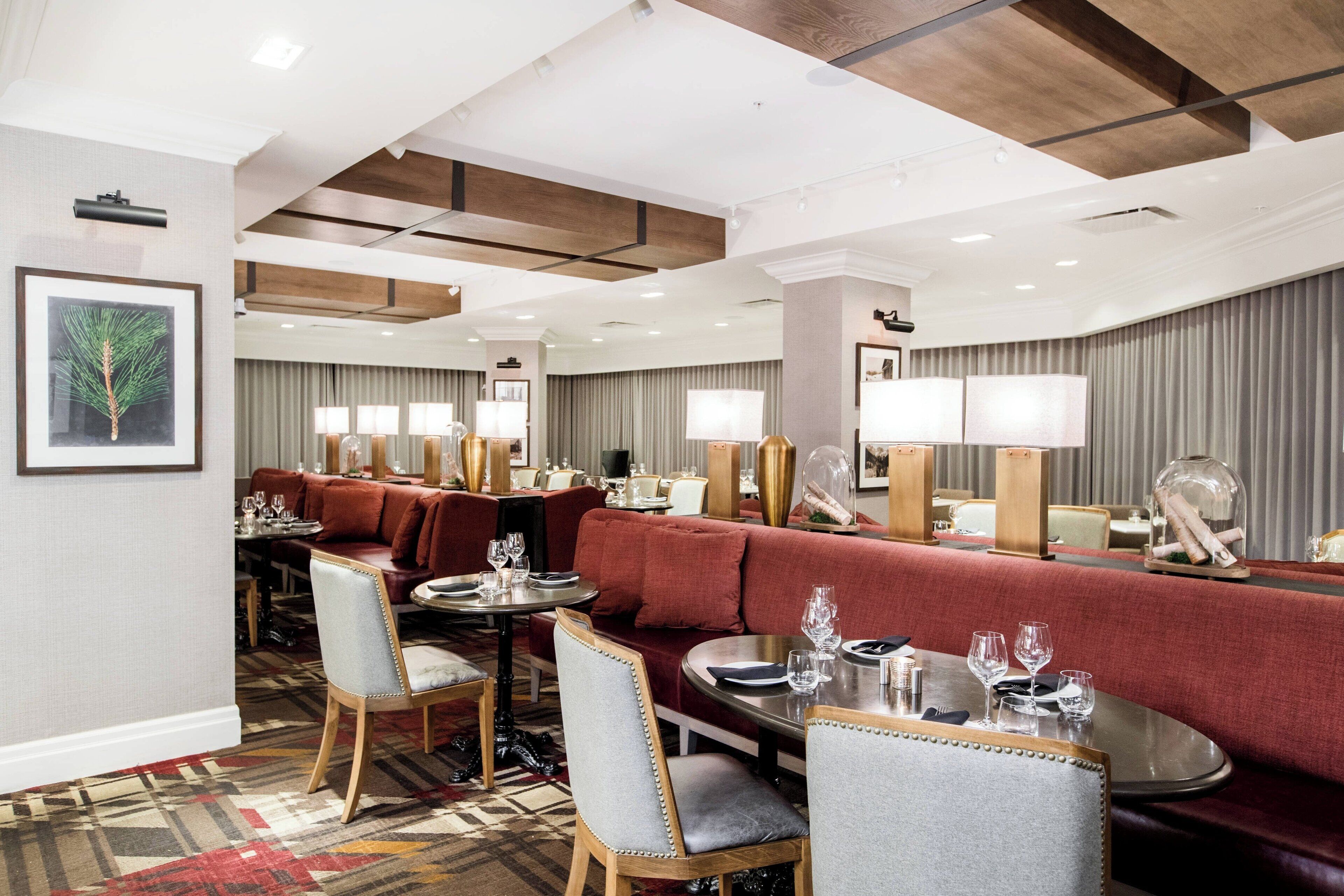 Eine Hotelhalle mit einem roten Sofa, Esstischen und Stühlen. An den Wänden befinden sich Bilder in Rahmen und der Boden ist mit Teppich ausgelegt.