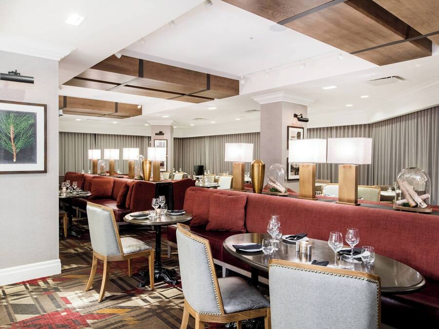 Eine Hotelhalle mit einem roten Sofa, Esstischen und Stühlen. An den Wänden befinden sich Bilder in Rahmen und der Boden ist mit Teppich ausgelegt.
