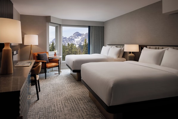 A hotel room with two beds, a desk, a chair, and a view of mountains. - Kananaskis Mountain Lodge, Autograph Collection (Kananaskis)