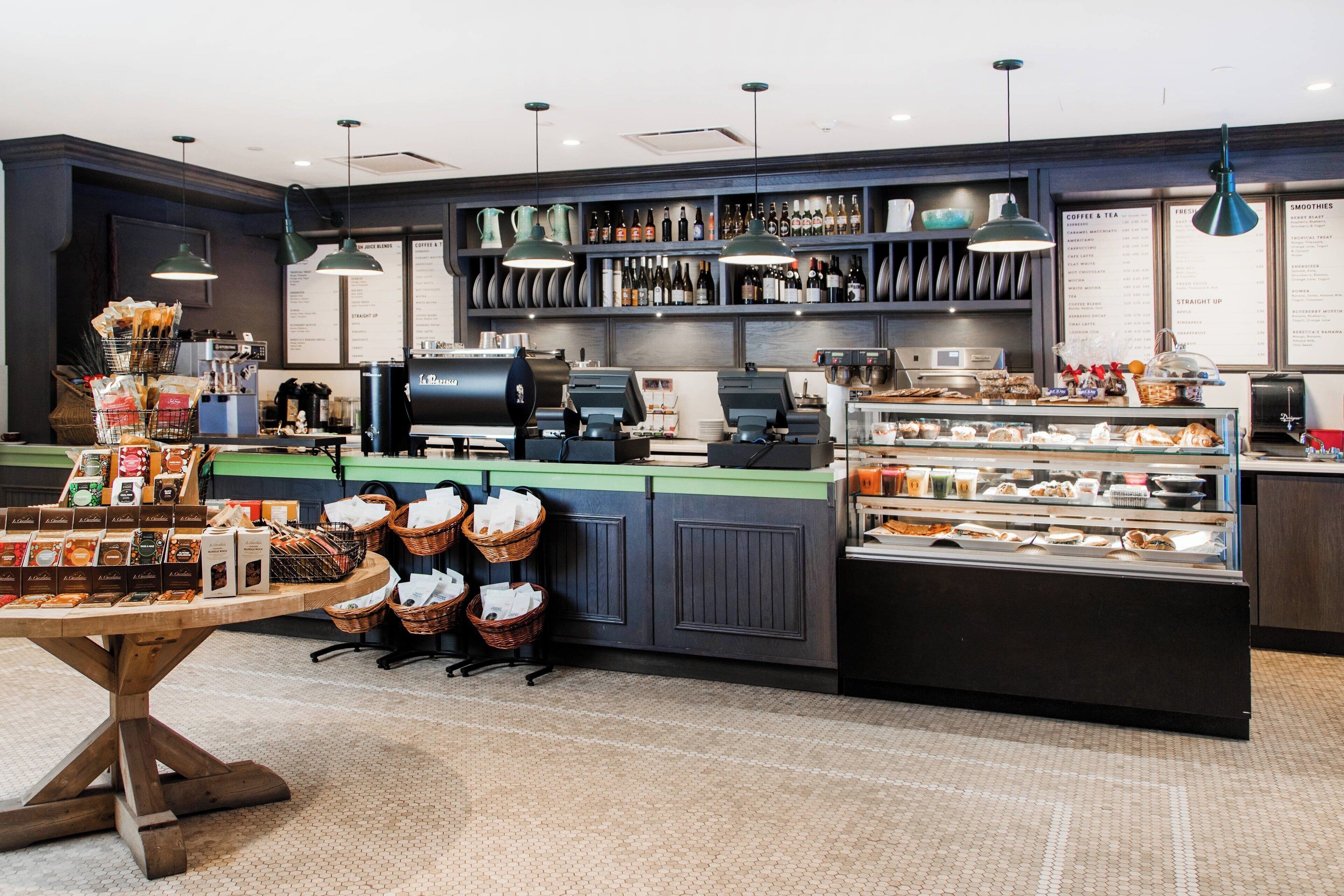 A coffee shop interior with a counter, coffee machines, a display case with pastries, and shelves with coffee and tea options.