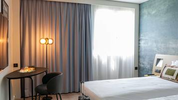 A hotel room with a bed, a desk with a chair, a suitcase, and a large window with curtains.
