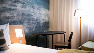 A hotel room with a bed, a small table, a chair, a lamp, and a wall with a textured pattern.