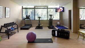 A gym with treadmills, an elliptical, a stationary bike, a purple exercise ball, and dumbbells.
