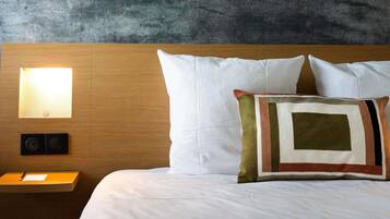 A neatly made bed with white linens, a wooden headboard, and a wall-mounted light fixture.