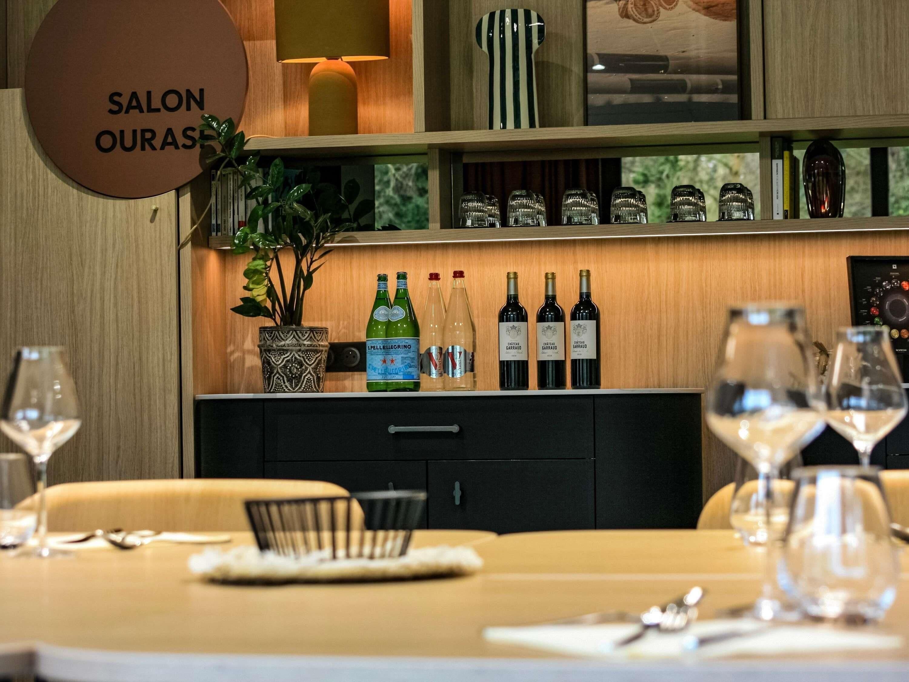 A restaurant interior with a wooden counter displaying wine bottles, a potted plant, and a sign reading 'SALON OURAS'.