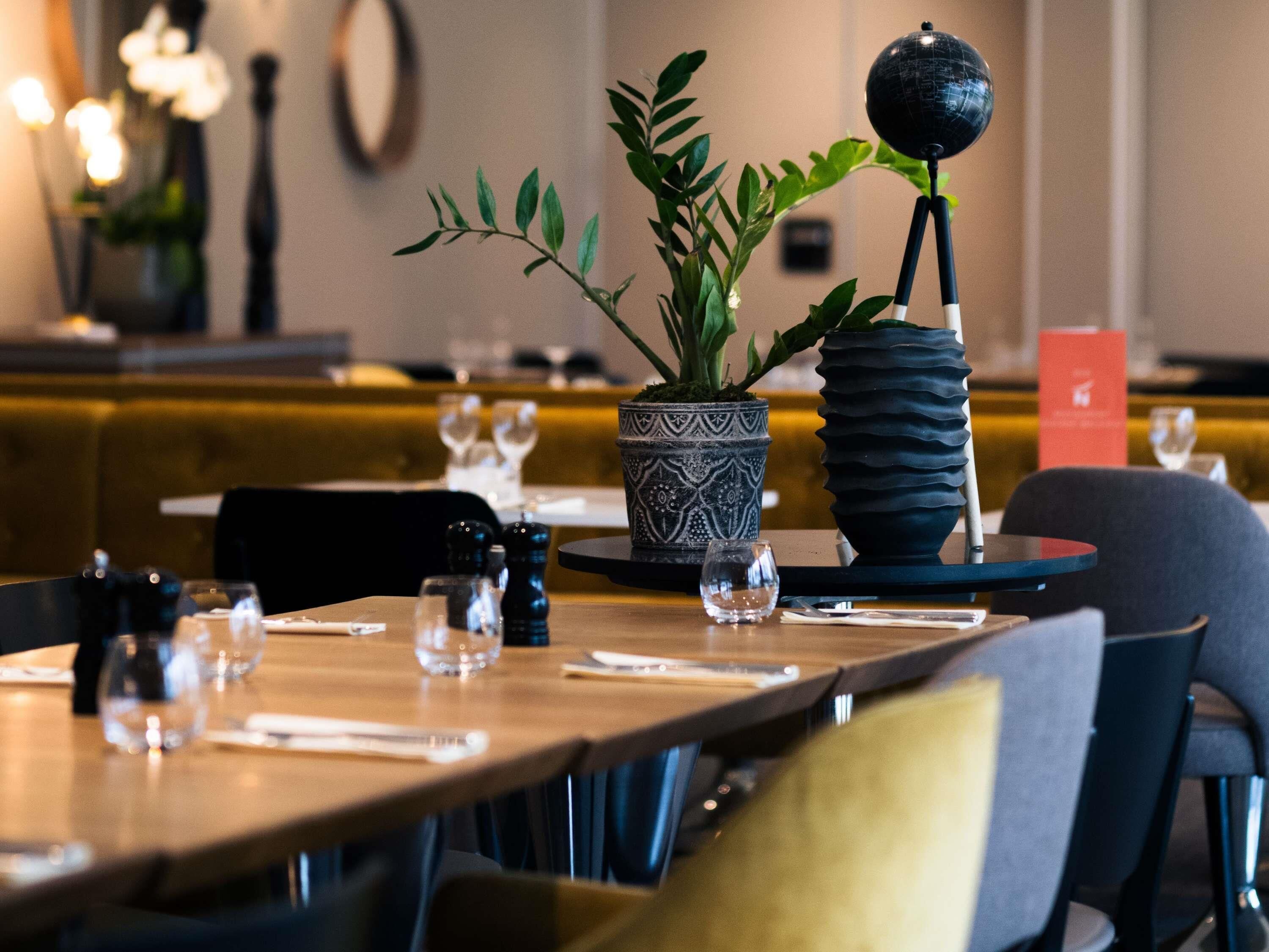 Interior de restaurante con mesas listas para comer, una planta en maceta y un globo decorativo sobre un atril.