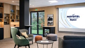 A modern hotel lobby with seating, a projection screen displaying the hotel name, and a view of the outdoors.