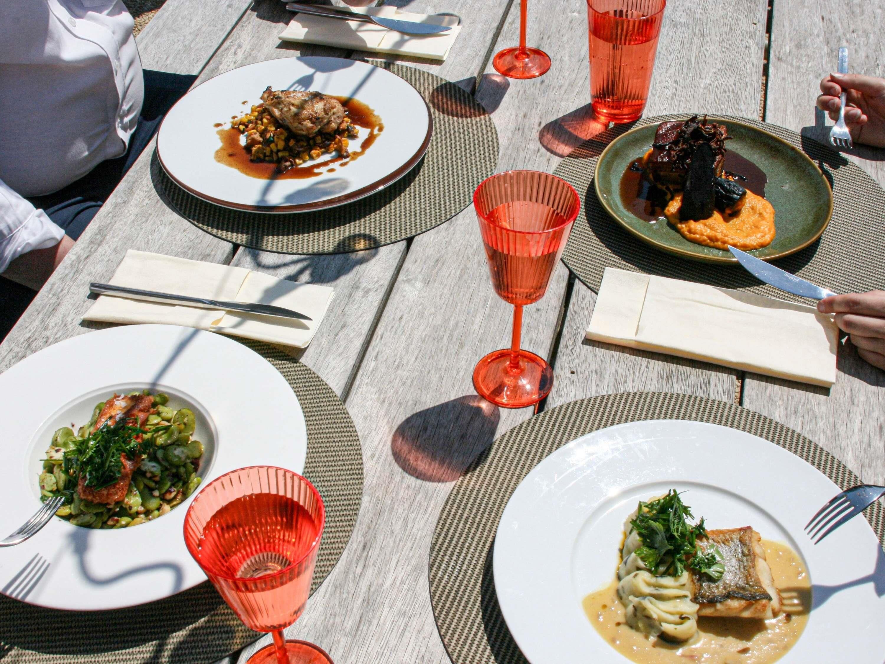 A dining table with plates of food, cutlery, and red glasses.