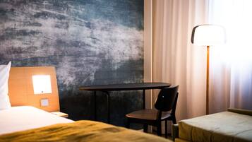 A hotel room with a bed, a small table, a chair, a sofa, and a lamp.