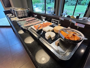 A buffet with various food items including salmon, cheese, and other meats. - Novotel Bayeux (Bayeux)