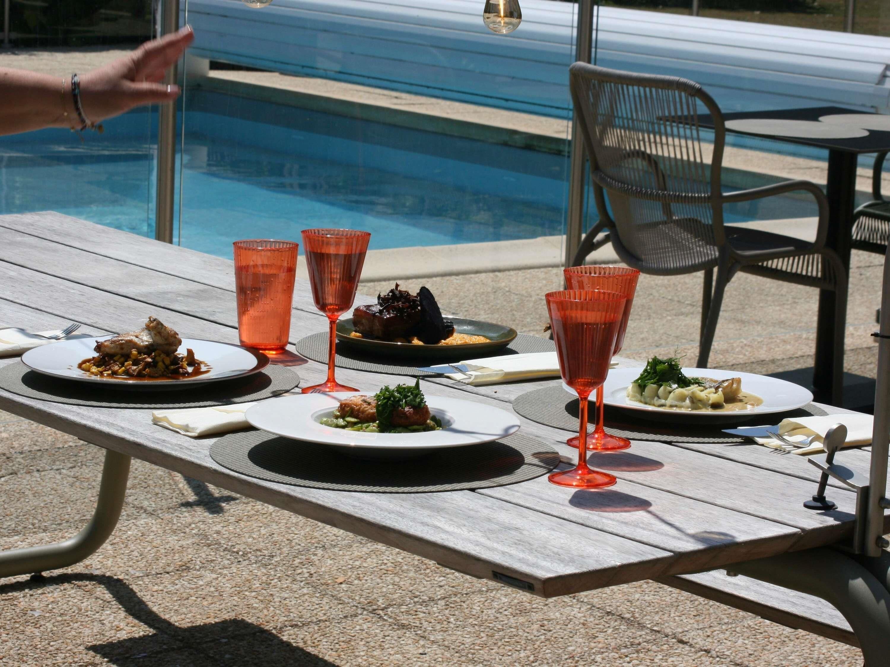 A dining table with plates of food and red glasses, near a pool.