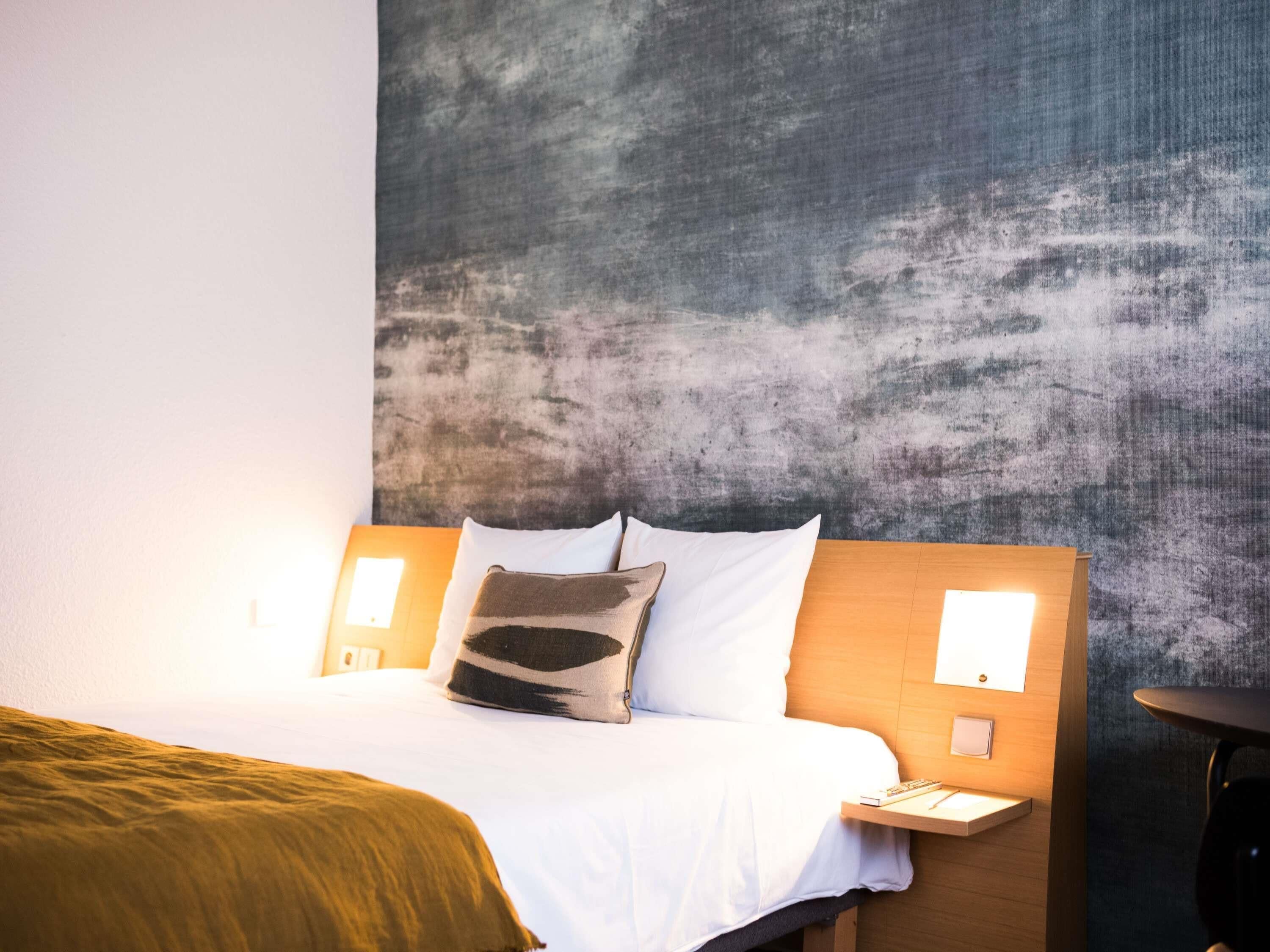 Habitación de hotel con cama, cabecero, mesitas de noche y una pared con textura.