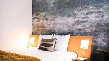 Habitación de hotel con cama, cabecero, mesitas de noche y una pared con textura.