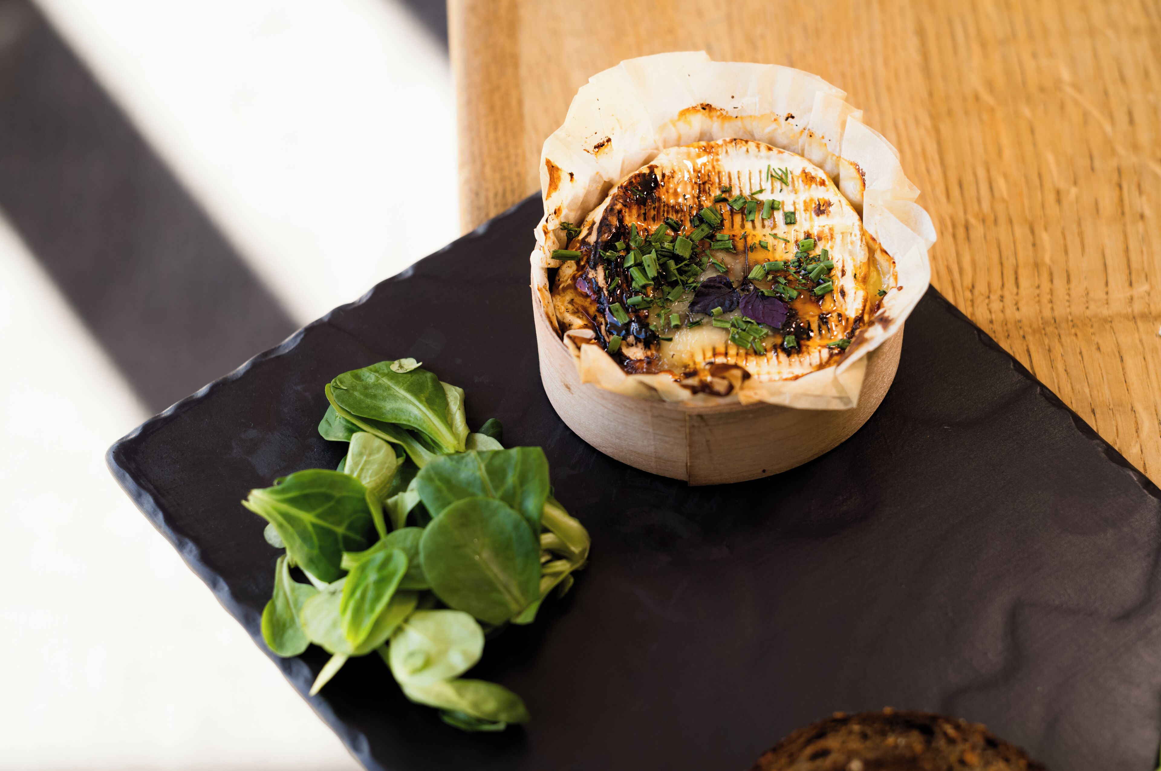 A dish of grilled cheese on a black plate with a wooden table in the background.